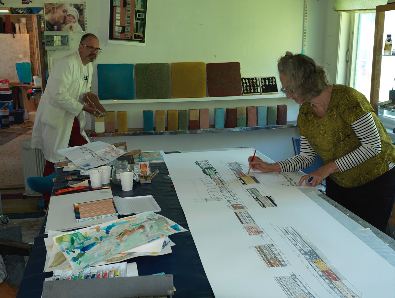To personer ved et arbeidsbord med skisser og fargeprøver.