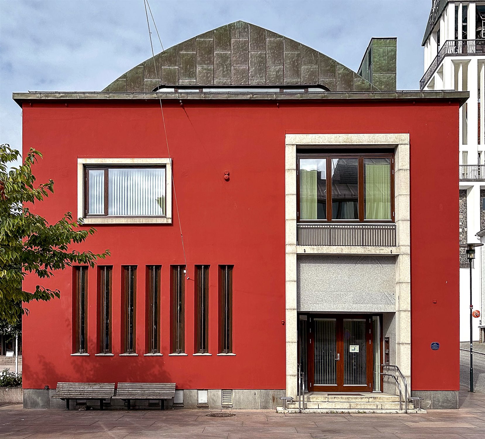 Rød, kvadratisk murbygning med teak vindu og dører med omramming. Foto.