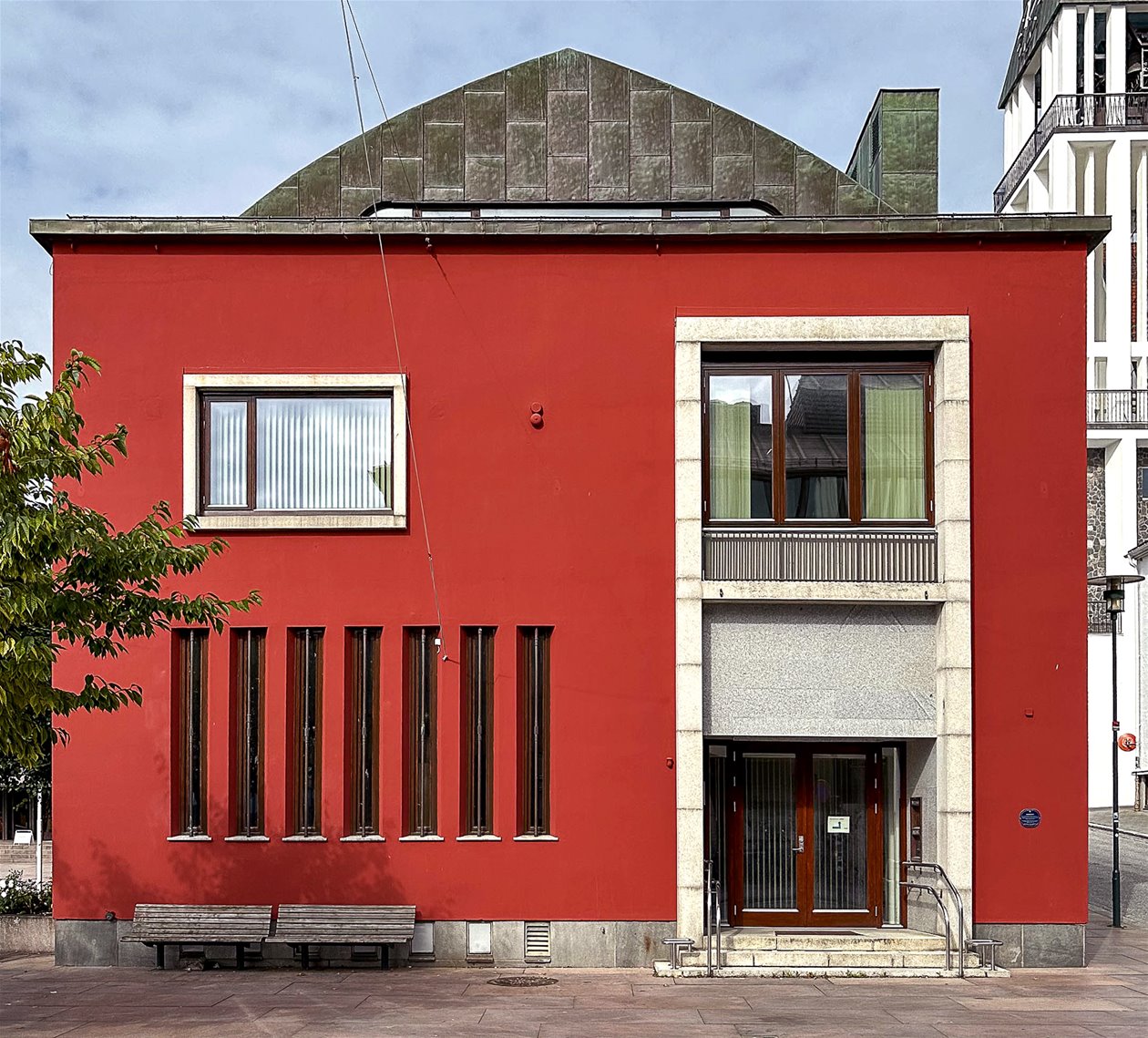 Rød, kvadratisk murbygning med teak vindu og dører med omramming. Foto.